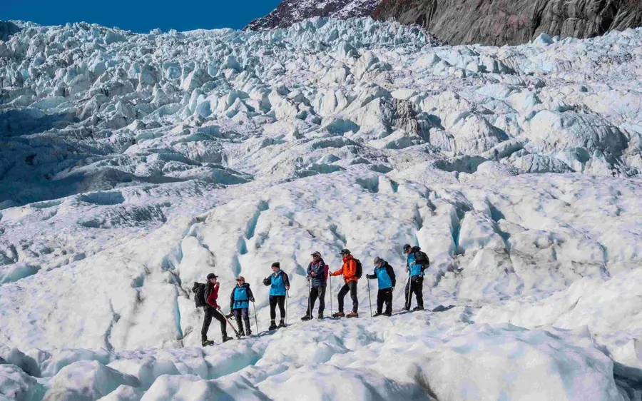 Hikers in crampons walking past an ice arch on Fox Glacier