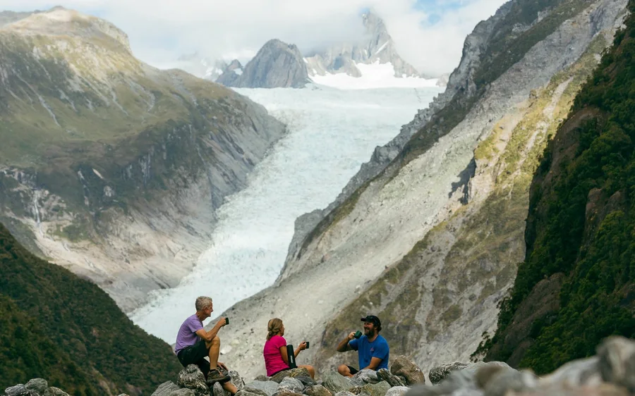 Walkers on the gravel track in the Fox Glacier valley below the ice