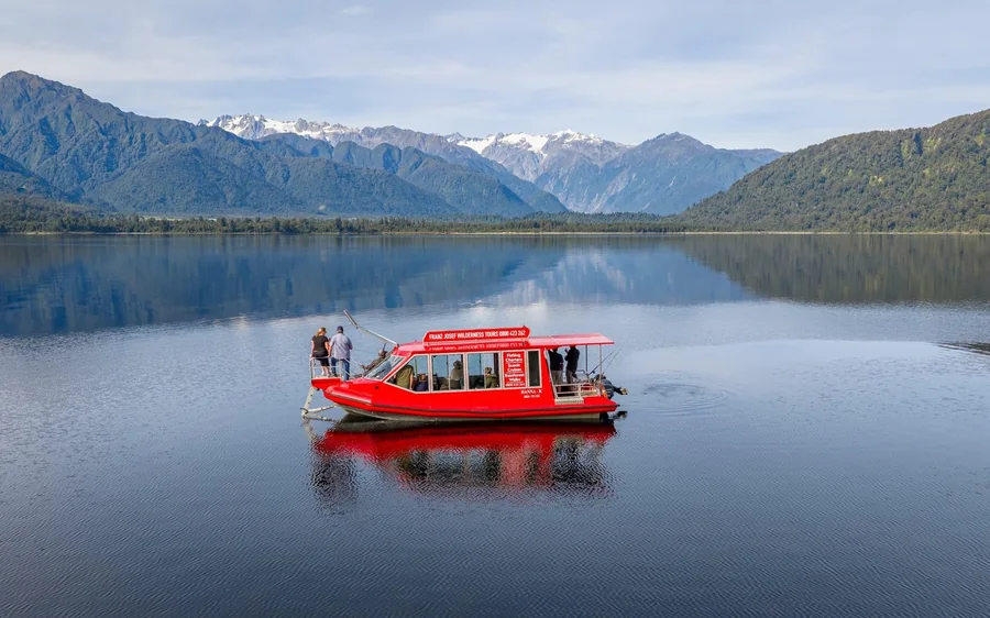 A small boat on Lake Mapourika with the Southern Alps behind it