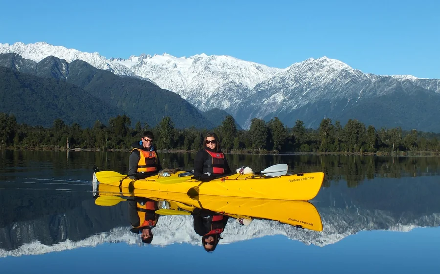 Kayakers paddling on the mirror-still water of Lake Mapourika