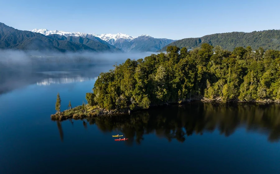 A kayak on the still water of Okarito Lagoon with forest behind
